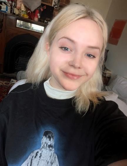 Portrait photo of SOYBOY producer Victoria Lincoln: white female, shoulder length bleach blonde hair, wearing a white turtleneck underneath a black t-shirt